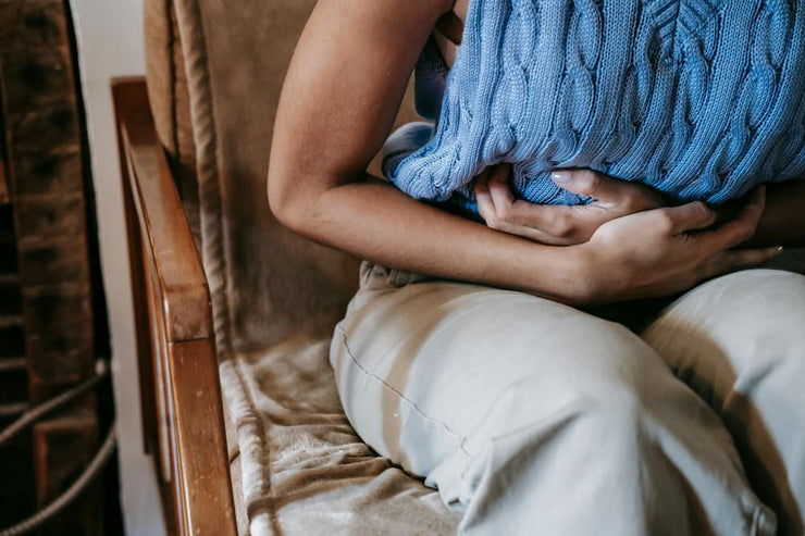 woman in blue top holding stomach in pain