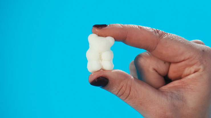 Small white CBD gummy bear being held on a blue background